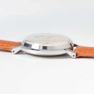 May include: A silver wristwatch with a white face and a brown leather band.