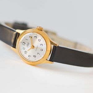 The tiny gold-plated watch on the woman’s wrist. The dial of the watch is with Arabic numerals, minimalist style, classic watch tiny little for every occasion. A piece of pre-owned vintage jewelry. You can make a better choice for the Planet.