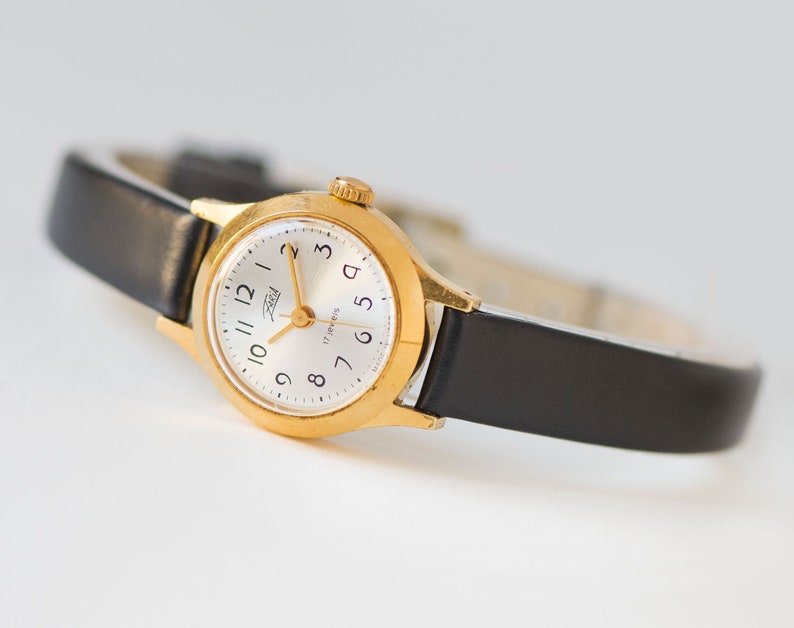The tiny gold-plated watch on the woman’s wrist. The dial of the watch is with Arabic numerals, minimalist style, classic watch tiny little for every occasion. A piece of pre-owned vintage jewelry. You can make a better choice for the Planet.