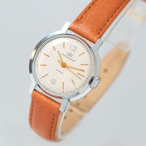 May include: A silver wristwatch with a white face and gold hands. The watch has a brown leather band and the words "Zlat. Moskovska" are printed on the face.