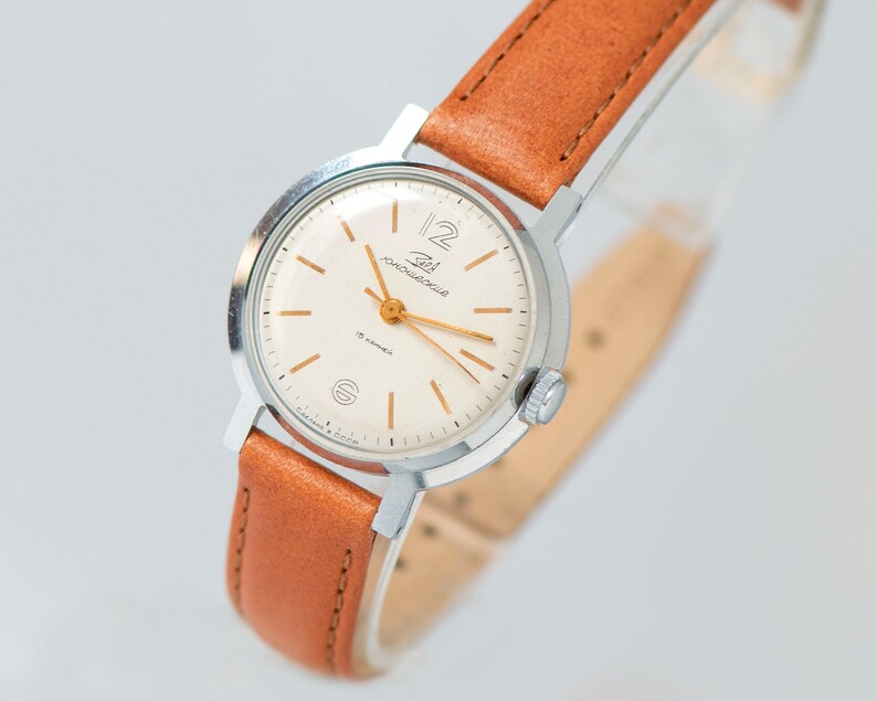 May include: A silver wristwatch with a white face and gold hands. The watch has a brown leather band and the words "Zlat. Moskovska" are printed on the face.