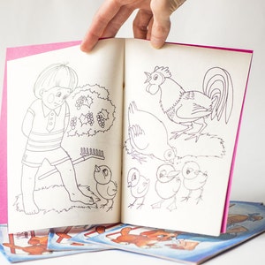 May include: A coloring book with a pink cover and black and white illustrations of a boy, a rooster, and chicks. The book is open to a page with a boy holding a rake and a rooster with chicks.