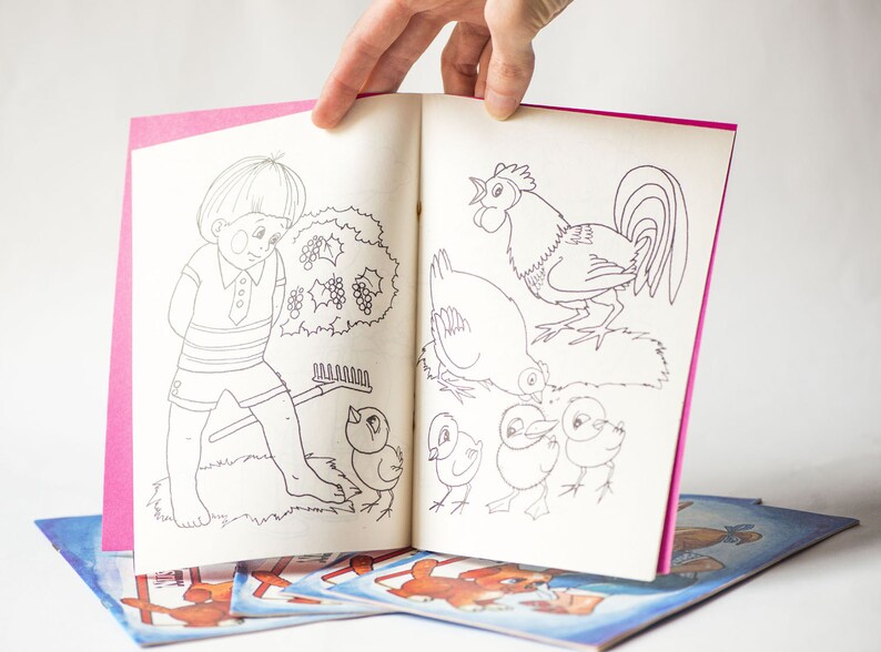 May include: A coloring book with a pink cover and black and white illustrations of a boy, a rooster, and chicks. The book is open to a page with a boy holding a rake and a rooster with chicks.