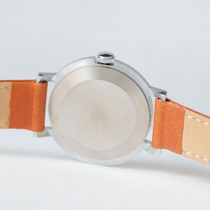 May include: A silver wristwatch with a round face and a brown leather band. The watch has a silver case and a silver band.