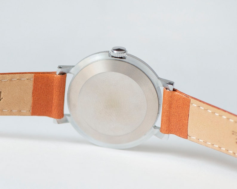 May include: A silver wristwatch with a round face and a brown leather band. The watch has a silver case and a silver band.