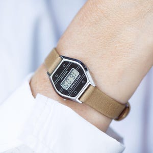 May include: A vintage digital wristwatch featuring a silver-toned hexagonal case and a tan leather strap. The black watch face displays the time in a digital format and includes the Cyrillic text "ЭЛЕКТРОНИКА 5" printed in white on the front.