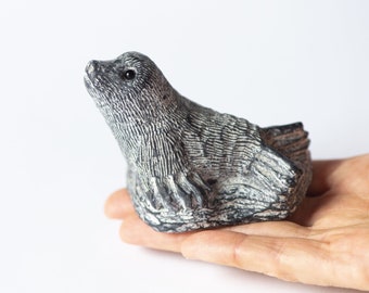 May include: A hand-carved stone sculpture of a seal, with a detailed, textured surface and a realistic pose. The seal is looking up, with its mouth slightly open.