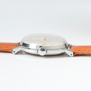 May include: A silver wristwatch with a white face and a brown leather band.