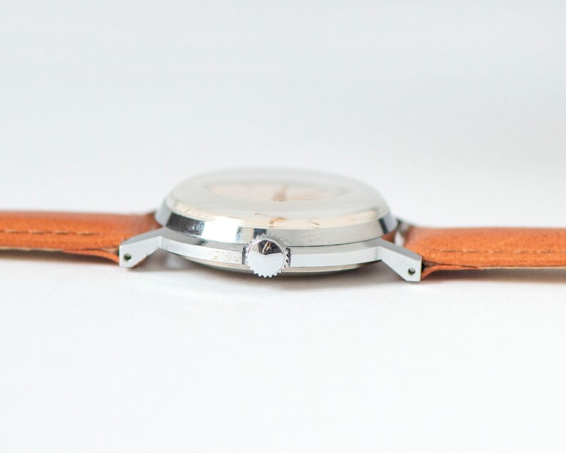 May include: A silver wristwatch with a white face and a brown leather band.