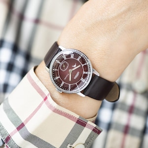 May include: A silver wristwatch with a brown leather band and a burgundy face. The face has Roman numeral hour markers and a small second hand.