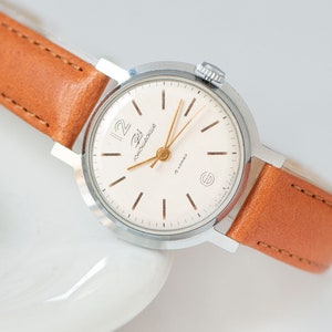 May include: A silver wristwatch with a white face and black markings. The watch has a brown leather band and says "Zlat 19 jewels" on the face.