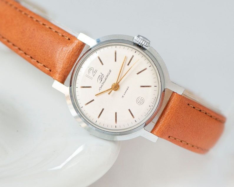 May include: A silver wristwatch with a white face and black markings. The watch has a brown leather band and says "Zlat 19 jewels" on the face.