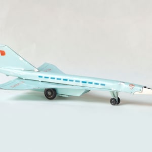 Pode incluir: Um avião de brinquedo azul claro com rodas pretas e marcas vermelhas e azuis. O avião tem a palavra "URSS" impressa no lado.