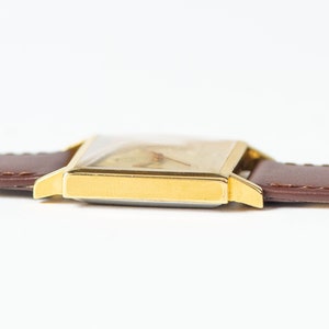 May include: A gold-toned wristwatch with a square face and a brown leather band.