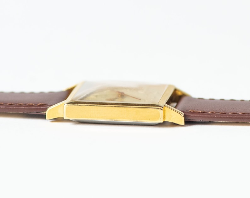 May include: A gold-toned wristwatch with a square face and a brown leather band.
