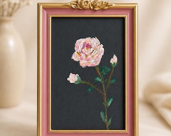 Op de afbeelding: Een rechthoekige fotolijst met een roze binnenrand en een gouden buitenrand, voorzien van een gouden roosornament aan de bovenzijde. Binnenin toont een zwart canvas een olieverfschilderij in impasto van een lichtroze roos met groene bladeren.