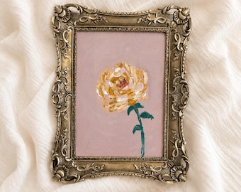 Op de afbeelding: Een rechthoekig schilderij met een enkele gele roos met zichtbare penseelstreken op een effen licht mauve achtergrond. Het kunstwerk is gevat in een sierlijke, antiek-stijl metallic gouden lijst met gedetailleerde bloemmotieven.