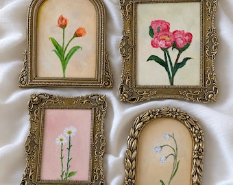 Op de afbeelding: Vier kleine rechthoekige en boogvormige wandlijsten in antieke goudkleurige afwerking, elk met een handgeschilderd bloemenkunstwerk. De schilderijen tonen oranje tulpen, roze pioenrozen, witte madeliefjes en kleine blauwe bloemen.