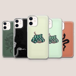 Könnte beinhalten: Fünf Smartphone-Hüllen in einer Reihe. Die erste ist olivgrün mit einer schwarzen Schlange und Rosen-Linienkunst. Die zweite ist schwarz mit einer weißen Schlange und Blumenmuster. Die dritte und vierte sind hellgrün mit einer geringelten grün-weißen Schlange. Die fünfte ist terrakottafarben mit der Silhouette einer schwarzen Schlange.