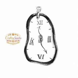 May include: A silver-toned pendant shaped like a melting clock with a white face, black Roman numerals for III, VI, IX, and XII, and black clock hands. The pendant features a dark, irregular border and a small silver loop at the top for attachment.