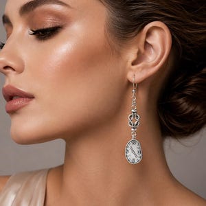 May include: A silver-toned drop earring featuring a dangling, irregular oval-shaped charm designed to resemble a melting clock face with visible numbers and hands. The earring is suspended from a silver hook and includes a decorative knot-like link.