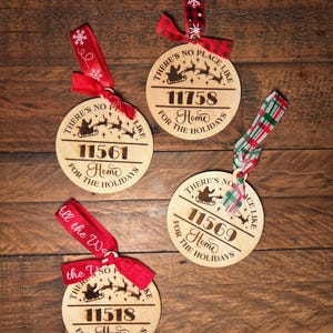Puede incluir: Cuatro adornos navideños de madera con cintas rojas. Cada adorno tiene un número de dirección único, la frase "There's no place like home for the holidays" y un diseño de trineo y renos.