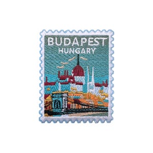 Puede incluir: Parche bordado con un diseño de Budapest, Hungría, que se asemeja a un sello postal. El parche muestra un puente, edificios y el texto "BUDAPEST HUNGARY" en blanco sobre un fondo turquesa, enmarcado por un borde azul claro.