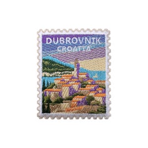 May include: Embroidered patch resembling a postage stamp, featuring the text "DUBROVNIK CROATIA." The patch depicts a coastal town with orange rooftops, a tall tower, and a mountain range, all under a purple and blue sky.
