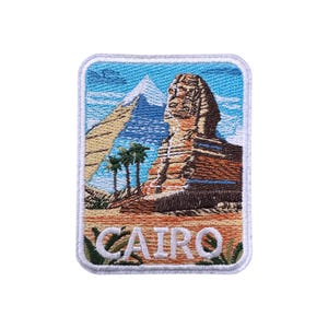 May include: Embroidered patch featuring the Sphinx and a pyramid against a blue sky. The patch includes palm trees and the word "CAIRO" in white letters. The patch has a white border.
