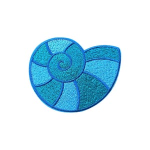 Puede incluir: Parche bordado con un diseño de concha estilizada. El parche presenta un patrón en espiral con diferentes tonos de azul, de claro a oscuro, creando una apariencia texturizada. El diseño está sobre un fondo blanco.