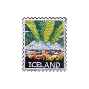 Puede incluir: Parche bordado con forma de sello postal que representa un colorido paisaje islandés. El diseño incluye montañas nevadas, un pueblo con tejados rojos y amarillos, y la palabra "ICELAND". El fondo representa una aurora boreal verde y amarilla.
