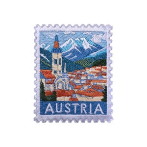 May include: Embroidered patch in the shape of a postage stamp depicting an Austrian landscape. The design shows a church, red-tiled roofs, mountains, and the word "AUSTRIA" in blue.