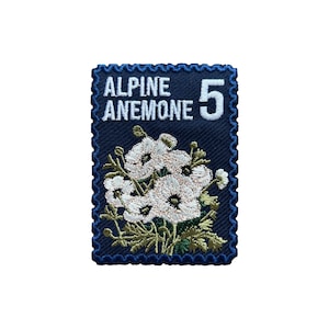 Puede incluir: Un parche bordado azul marino con diseño de sello postal. El parche presenta las palabras "ALPINE ANEMONE" y el número "5" en blanco. El centro del parche muestra un grupo de flores blancas con hojas verdes.