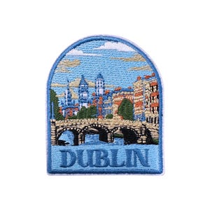 Könnte beinhalten: Gestickter Aufnäher mit einer Dublin-Szene. Das Design zeigt eine Brücke, Gebäude und das Wort "DUBLIN" in Blau. Der Aufnäher hat einen blauen Rand und einen hellblauen Himmel, ideal zum Aufnähen auf Kleidung.