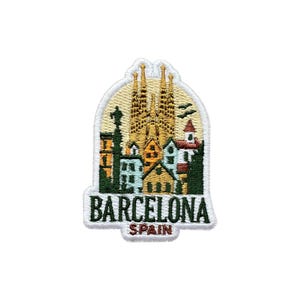 Op de afbeelding: Geborduurde patch met de skyline van Barcelona, inclusief de Sagrada Familia. De patch heeft een crèmekleurige rand en de tekst "BARCELONA SPAIN" in het wit. Ideaal voor reisliefhebbers en souvenirverzamelaars.