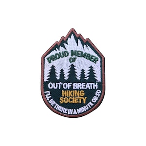 May include: A patch with a mountain and tree design, featuring the text "PROUD MEMBER OF OUT OF BREATH HIKING SOCIETY". The patch also includes the phrase "I'LL BE THERE IN A MINUTE OR SO" in a curved font.