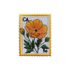 May include: Embroidered patch featuring a vibrant orange poppy flower with green leaves and buds, resembling a postage stamp. The patch has a white background with the letters "CA" and the number "5¢" in the corners, framed by a yellow border.