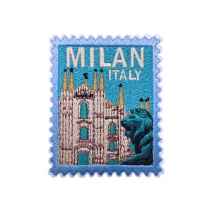 May include: Embroidered patch in a light blue postage stamp design, with the text "MILAN ITALY". The patch shows a detailed illustration of a cathedral and a statue in shades of white, beige, and teal.