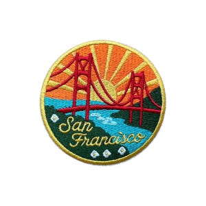 May include: Embroidered patch featuring the Golden Gate Bridge in San Francisco. The design includes a red bridge, a setting sun, and the words "San Francisco" in a cursive font. The patch has a yellow border and a green and blue landscape.