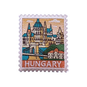 May include: Embroidered patch featuring a colorful depiction of a cityscape, resembling a postage stamp. The design includes buildings, bridges, and the word "HUNGARY" in orange. The patch has a scalloped border and is set against a white background.