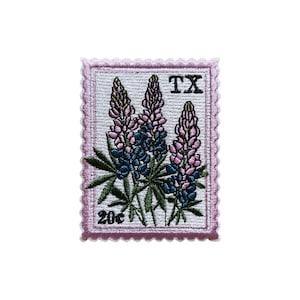 May include: Embroidered patch featuring three bluebonnet flowers in shades of blue and purple, with green leaves. The patch is in the shape of a postage stamp, with the text "TX" and "20¢". The border is a light pink.
