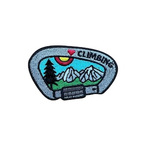 May include: Embroidered patch in the shape of a climbing carabiner. The patch features a mountain scene with a tree, sun, and the word "CLIMBING". The design includes a red heart and is outlined in gray.