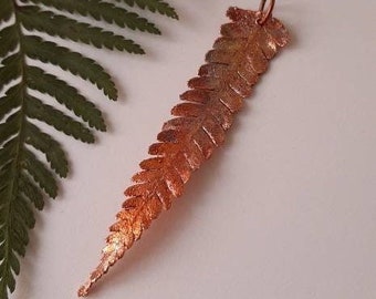 Op de afbeelding: Een koperen varen hanger met een gedetailleerd ontwerp. De hanger is een enkele varen frond met een textuur.