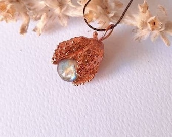 Op de afbeelding: Een koperen ketting met een delicate, getextureerde hanger die lijkt op een bloemknop. De hanger heeft een ronde, iriserende edelsteen in het midden.