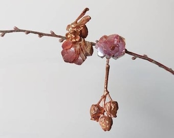 Op de afbeelding: Een paar roze en gouden kristallen oorbellen die aan een tak hangen. De oorbellen zijn gevormd als trossen van kleine kristallen.