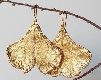 Op de afbeelding: Gouden oorbellen in de vorm van ginkgo bladeren, hangend aan een tak.
