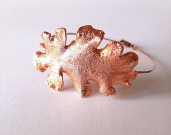 Op de afbeelding: Een koperen armband met een bladvormig ontwerp en een dunne draadband.