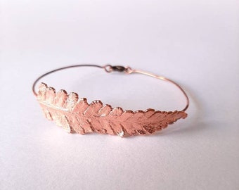Op de afbeelding: Een delicate koperen armband met een varenblad ontwerp. De armband is gemaakt van dunne draad en heeft een eenvoudige, elegante uitstraling.