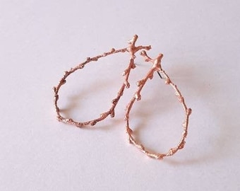 Op de afbeelding: Een paar oorbellen van roségoud in de vorm van delicate takken met kleine bladeren.