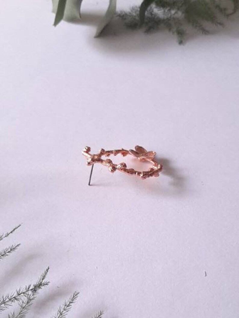 Pu&ograve; includere: Un orecchino a forma di ramo in oro rosa con un delicato design a farfalla. L'orecchino &egrave; in metallo e ha un retro a perno.